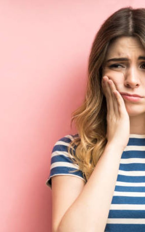 Young Caucasian woman suffering from dental illness isolated over coral background